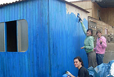 Tres voluntarias pintan de azul una de las viviendas construidas.